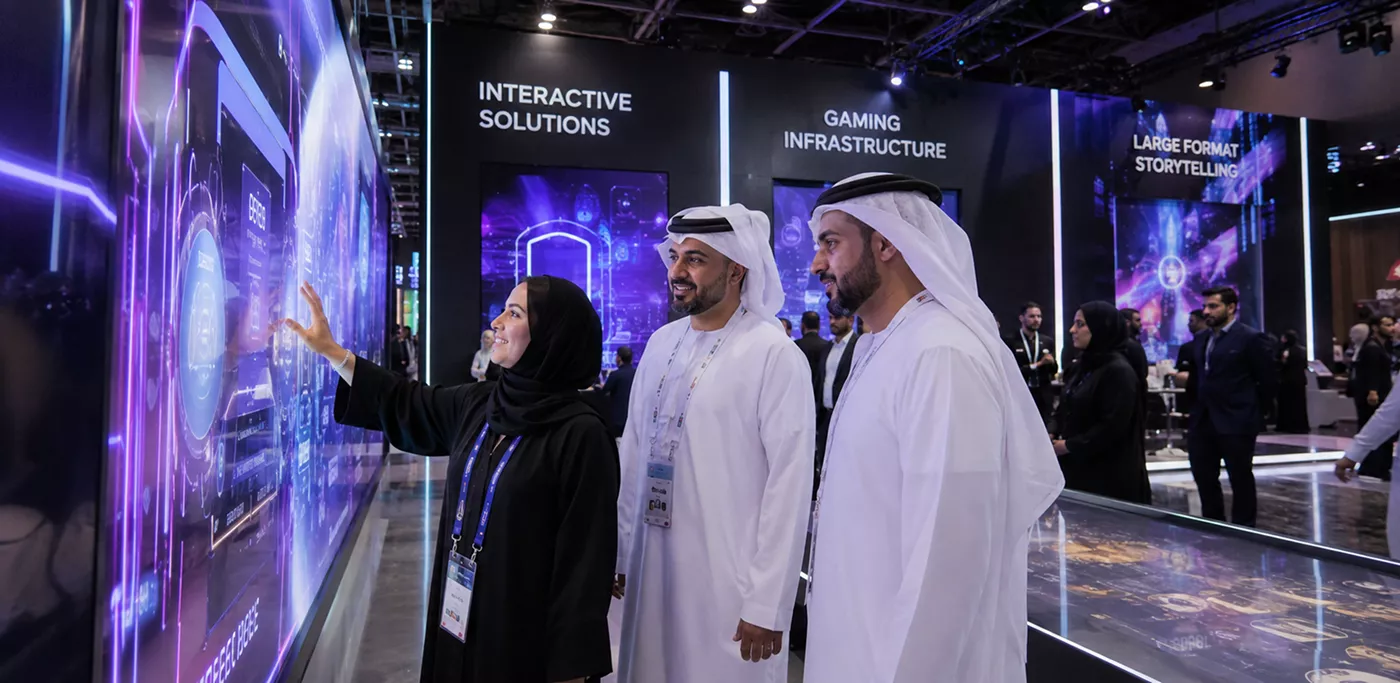 two-men-in-traditional-emirati-dress-and-a-woman-view-an-interactive-digital-wall-showcasing-gaming-infrastructure-and-large-format-storytelling-solutions
